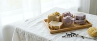 Handmade natural soap bars with lavender and herbs displayed on wooden tray, artisan skincare products for spa and wellness routines.