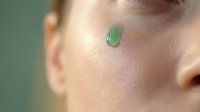 Young woman applying green skincare serum drop on face for natural beauty routine and healthy glowing skin care treatment.