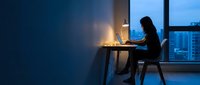 Young Asian businesswoman working late at office desk with laptop computer by window overlooking city skyline at night for productivity and career success.