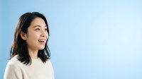 Young Asian woman with shoulder-length dark hair wearing a cream-colored sweater, smiling and looking to the side against a light blue background. Portrait suitable for business, lifestyle, and wellness content.