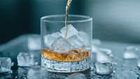 Pouring golden liquid into crystal glass with ice cubes on dark background, dynamic splash moment captured in luxury beverage photography.