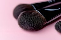Soft makeup brush bristles in macro view against pink background, professional cosmetic tool with black handle showing fine detailed texture and fibers.