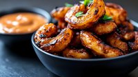 Grilled spicy shrimp in black ceramic bowl with creamy sauce. Close up view of seafood appetizer garnished with fresh herbs against dark background.