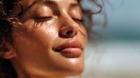 Young mixed race woman with glowing skin and closed eyes enjoying sunlight, natural beauty with dewy complexion and serene expression against blurred background.
