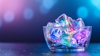 Glowing ice cubes in glass bowl with vibrant neon pink and blue lighting effects against dark background, creating magical atmosphere for beverage photography.