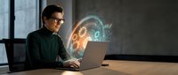 Professional businessman with glasses working on laptop with holographic brain and digital interface projections in modern office environment.