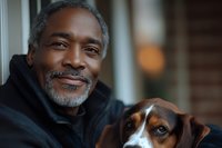 Mature African American man with gray beard smiling warmly while embracing his brown and white beagle dog outdoors, expressing joy and companionship in natural lighting.