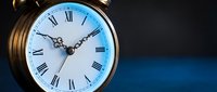 Vintage brass alarm clock with Roman numerals glowing with blue light on dark background, symbolizing time management and urgency.