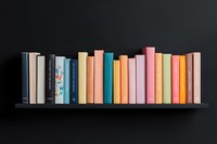 Row of colorful hardcover books arranged on black floating shelf against dark wall, featuring pastel and muted tones creating minimalist aesthetic display.