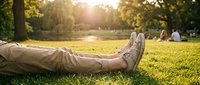 Person relaxing on green grass in sunny park with golden sunlight filtering through trees during peaceful outdoor leisure time.