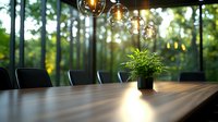 Modern conference room with wooden table, pendant glass lights and potted plant against panoramic forest view window, creating serene business atmosphere.