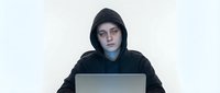 Young Caucasian male hacker in black hoodie working on laptop computer against white background for cybersecurity and technology concepts.