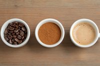 Three stages of coffee preparation: whole roasted beans, ground powder, and brewed espresso in white cups on wooden surface.