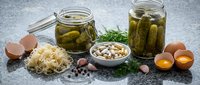 Fermented foods collection with pickled cucumbers in jars, sauerkraut, nuts and fresh eggs on granite counter for healthy probiotic nutrition and cooking.