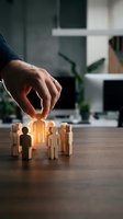 Business hand selecting glowing wooden figure from group on office desk representing talent recruitment and team leadership in corporate environment.