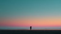 Romantic couple silhouette on beach at sunset with colorful sky gradient from turquoise to coral pink, peaceful ocean horizon for wedding and love concepts.