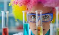 Young female scientist in protective eyewear examining colorful chemical reactions in laboratory test tubes against vibrant smoke background, demonstrating research curiosity.