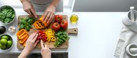 Hands preparing fresh colorful vegetables on wooden cutting board in modern kitchen. Healthy cooking and meal preparation concept for family dinner.