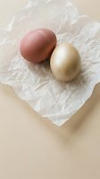 Two naturally colored eggs on crumpled parchment paper against neutral beige background for Easter cooking and baking projects.
