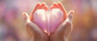 Gentle hands cupping a glowing pink origami heart against a soft bokeh background, symbolizing love, care, and emotional connection.