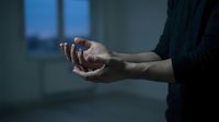 Caucasian man holding his wrist in pain in a dark empty room, expressing discomfort, injury, or stress in a moody blue-toned setting.