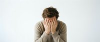 Young man covering face with hands showing stress, depression, anxiety or mental health struggles isolated on white background for wellness concepts.