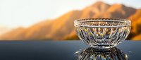 Crystal glass bowl with intricate cut patterns on reflective surface, golden mountain sunset backdrop, luxury tableware elegance.