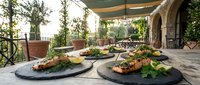 Gourmet appetizers elegantly plated on dark slate boards displayed on outdoor terrace with Mediterranean architecture and lush greenery for upscale dining.