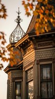 Victorian house with ornate iron cupola and decorative trim bathed in warm autumn sunlight through colorful fall foliage creating architectural shadows.