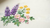 Delicate hand embroidered wildflower bouquet with purple lavender, yellow buttercups and pink roses on cream fabric for crafting and textile projects.