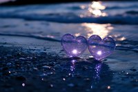 Two purple crystal hearts on wet beach sand reflecting golden sunset light creating romantic atmosphere for love and relationship concepts.