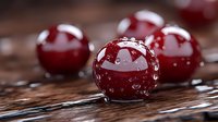 Fresh ripe cherries with water drops on dark wooden background, macro shot showing juicy texture and natural gloss of wet fruit surface.