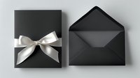 Black gift box with elegant white satin bow and matching open black envelope on neutral background, minimalist luxury presentation for special occasions.