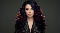 Young woman with long, voluminous burgundy and black ombre waves, fair complexion, wearing dark patterned jacket against neutral background for beauty and fashion use.
