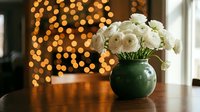 White roses in green ceramic vase on wooden table with warm bokeh lights background creating cozy home interior atmosphere for romantic decor.