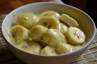 Fresh sliced bananas in creamy vanilla pudding dessert served in white ceramic bowl, close up view of sweet homemade comfort food with smooth texture.