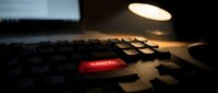 Close-up of computer keyboard with glowing red Cancel key under warm desk lamp light. Dark moody workspace atmosphere for technology and business concepts.