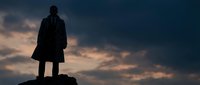 Silhouette of a man standing on a rock against dramatic sunset sky with orange and blue clouds, representing leadership, ambition, and success in business and personal growth.