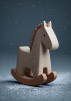 Wooden rocking horse toy on dark background with falling snow effect. Handcrafted children's nursery decoration for winter holiday season.
