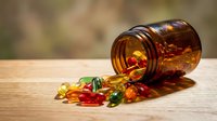 Colorful vitamin capsules and pills spilling from amber glass bottle on wooden surface for health and wellness supplement concepts.