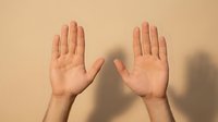 Two open hands raised up showing palms in stop gesture or surrender pose against neutral beige background with soft shadow for communication concepts.