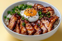Asian style rice bowl with grilled teriyaki chicken, sunny side up egg, green onions and sesame seeds served on steamed white rice in ceramic bowl.