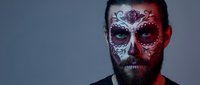 Bearded man with elaborate Day of the Dead sugar skull face paint featuring intricate floral patterns and decorative elements for Halloween costume makeup.