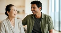 Two diverse young adults smiling while having a friendly conversation indoors, suitable for lifestyle, relationship, communication and workplace themes.