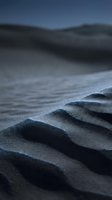 Close-up of rippled sand dunes with shallow depth of field, showcasing textured patterns and shadows in cool blue tones for nature and landscape backgrounds.