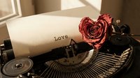Vintage typewriter with paper typed Love and a dried red rose shaped as heart, romantic retro concept for Valentine's Day cards and posters.