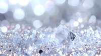 Sparkling ice crystal macro on glittering silver surface with soft bokeh background creates magical winter atmosphere for seasonal designs and holiday cards.
