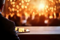 Person sitting alone at wooden table with blurred golden bokeh lights creating atmospheric mood. Contemplative moment in restaurant or cafe setting.