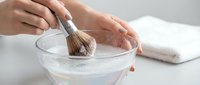 Woman hands mixing homemade face mask in glass bowl with brush for natural skincare routine and beauty treatment at home spa.
