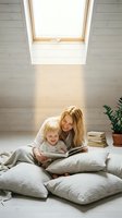 Young Caucasian mother and toddler reading a book together on floor cushions in a bright attic room with skylight natural light.